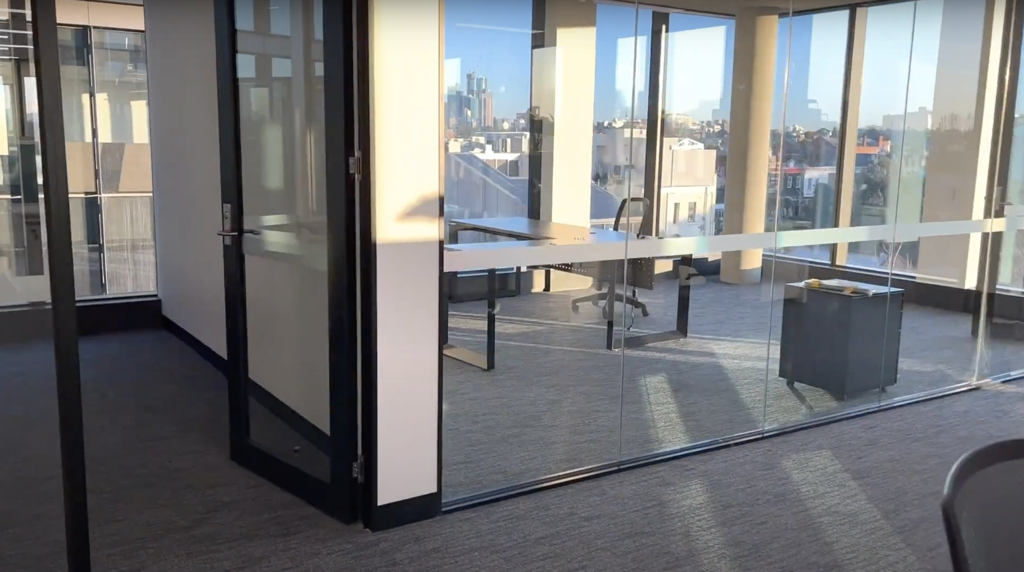 Bright, glass-walled open-plan office with floor-to-ceiling windows overlooking a sunny city skyline